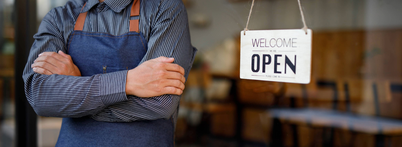 Man crossing arms with Welcome We Are Open sign